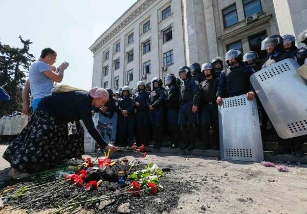 Woman lays flowers as members of the Ukrainian Interior Ministry security forces stand guard outside a trade union building in Odessa