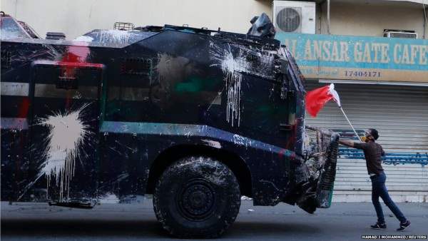 Протестующий, держа  флаг Бахрейна, противостоит бронетранспортеру, принадлежащему полиции. 
