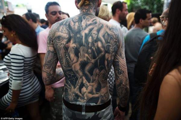 Мужчина на фестивале, чья спина покрыта тату с обнаженными женщинами.